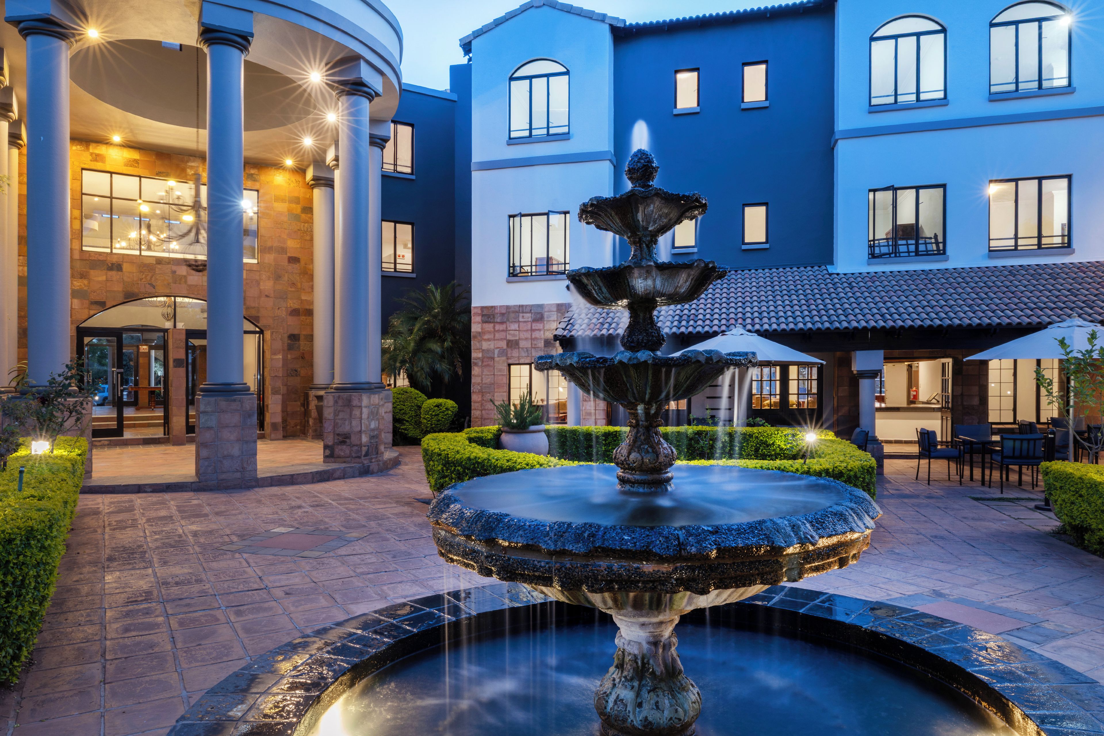 Un patio con una fuente central, un edificio con múltiples ventanas y un seto bien cuidado.