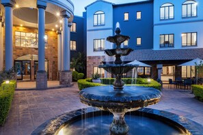 A courtyard with a central fountain, a building with multiple windows, and a well-maintained hedge. - Basden Wood Hotel Pty Ltd (Centurion)