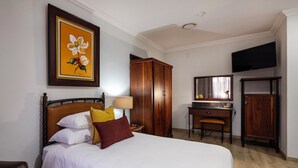 Habitación de hotel con cama, escritorio, armario, televisor y un cuadro en la pared.