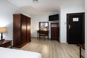 Una habitación de hotel con cama, escritorio con silla, armario, televisor y puerta.