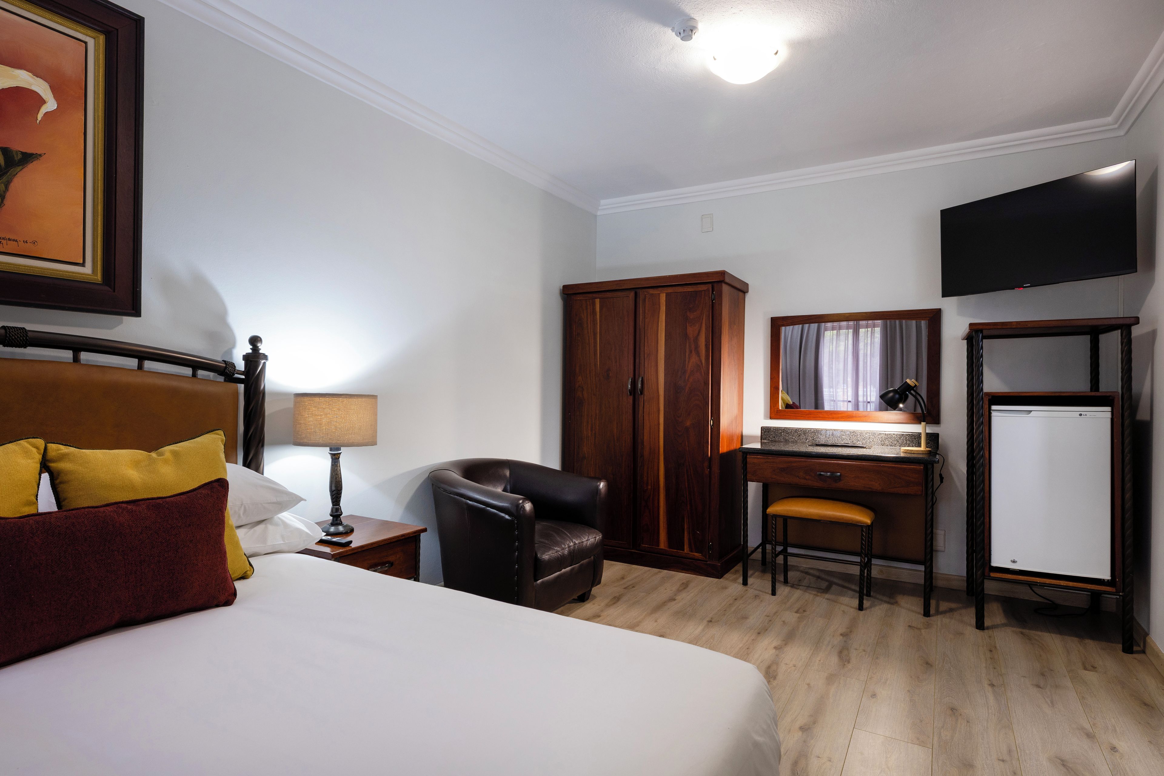 A hotel room with a bed, a desk, a chair, a wardrobe, a television, and a refrigerator.