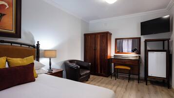 A hotel room with a bed, a desk, a chair, a wardrobe, a television, and a refrigerator.