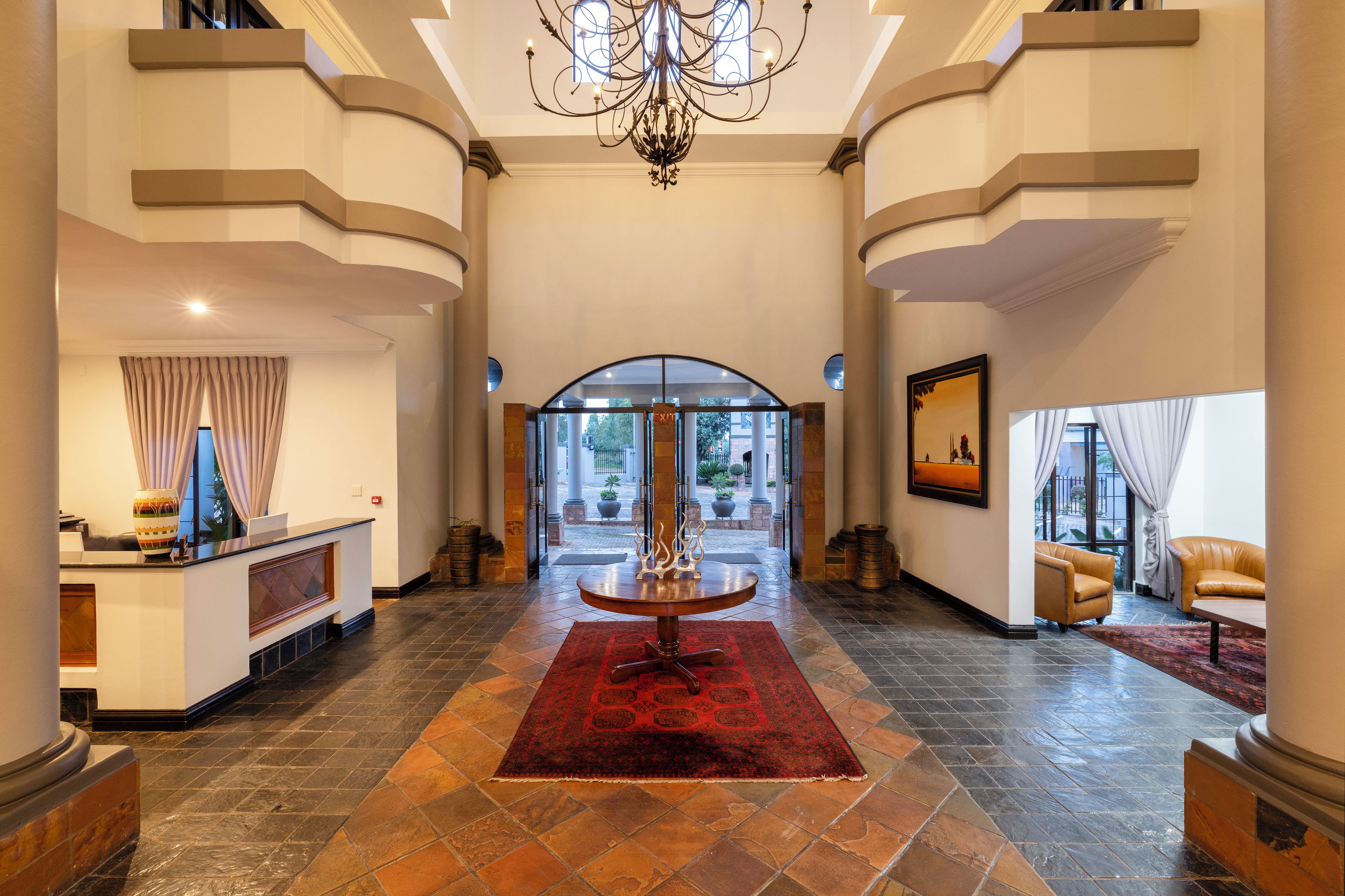 Un vestíbulo imponente con una mesa de recepción, un candelabro, una alfombra roja y vistas a través de un cristal.