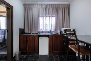 Una cocina compacta con armarios de madera, un lavavajillas blanco, un microondas y un comedor con mesa y sillas de madera.
