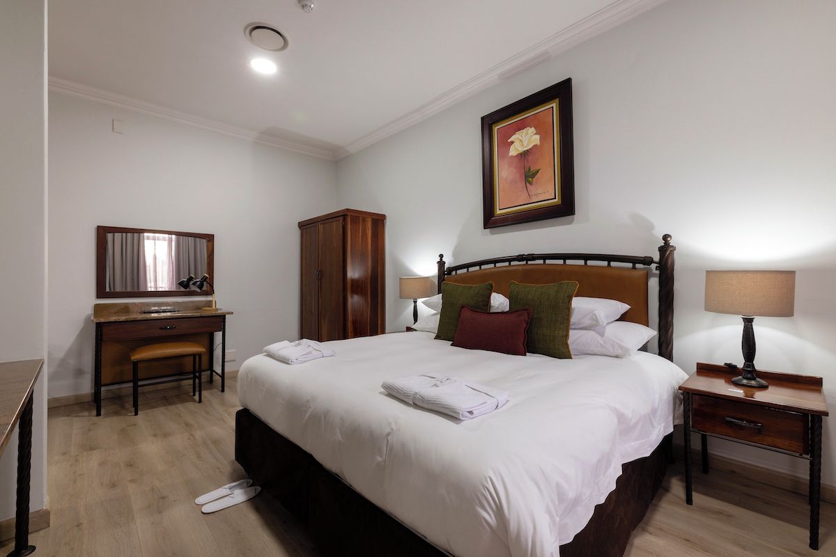 A hotel room with a bed, bedside tables, a desk, a mirror, and a framed picture on the wall.
