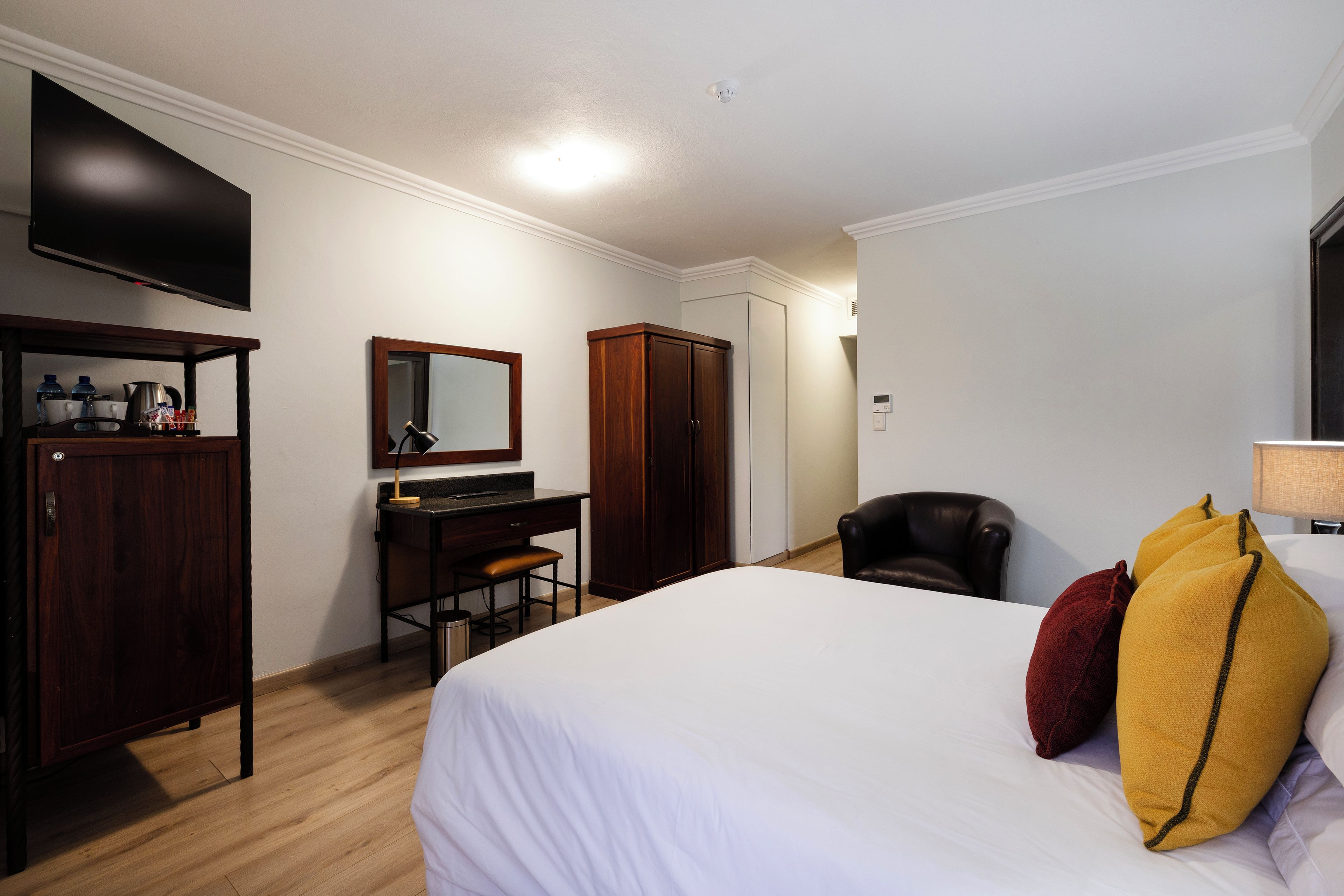 A hotel room with a bed, a desk, a chair, a wardrobe, a television, and a mirror.
