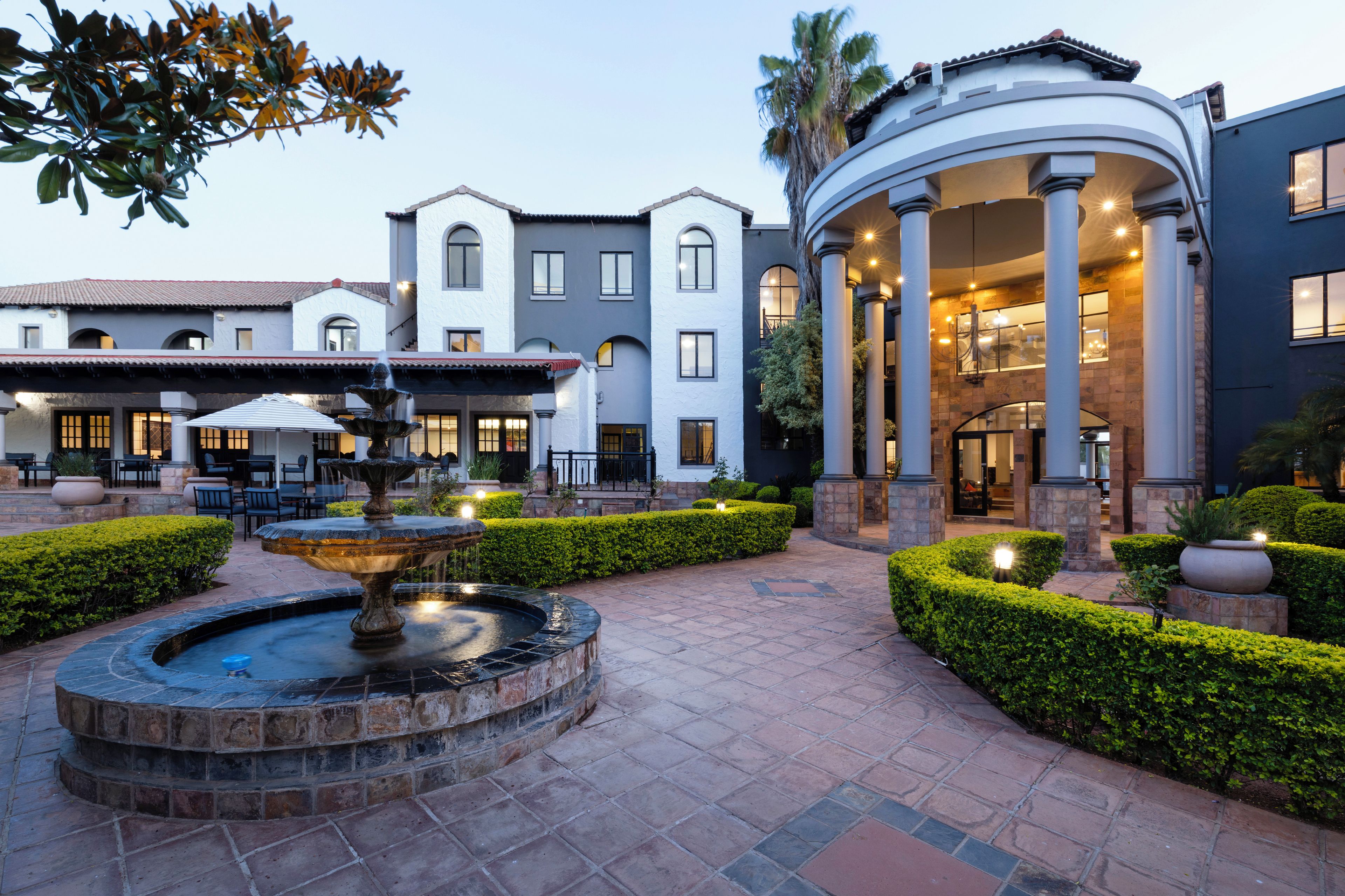 A courtyard with a fountain, seating area, and a building with columns and a covered entrance.
