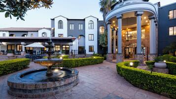 A courtyard with a fountain, seating area, and a building with columns and a covered entrance.