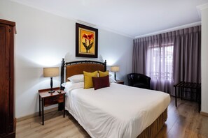 Habitación de hotel con una cama grande, dos mesitas de noche, una silla, una ventana con cortinas y un cuadro en la pared.