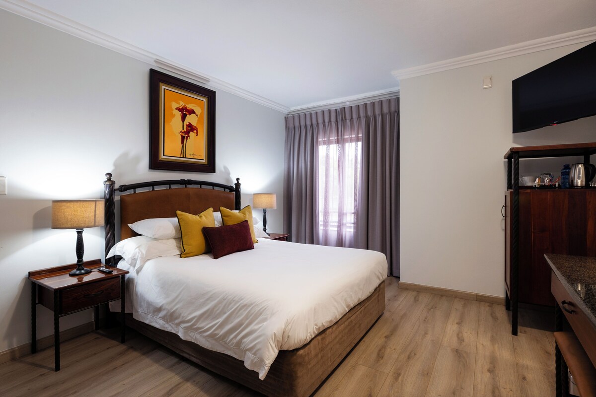 Una habitación de hotel con una cama, mesitas de noche, un televisor y un cuadro en la pared.