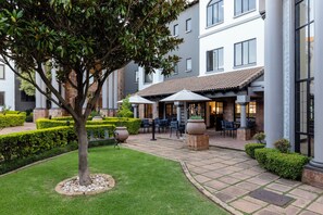 Un patio con un árbol, asientos al aire libre y un edificio con ventanas amplias.