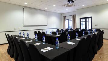 A conference room with long tables, black chairs, water bottles, and a projector screen.