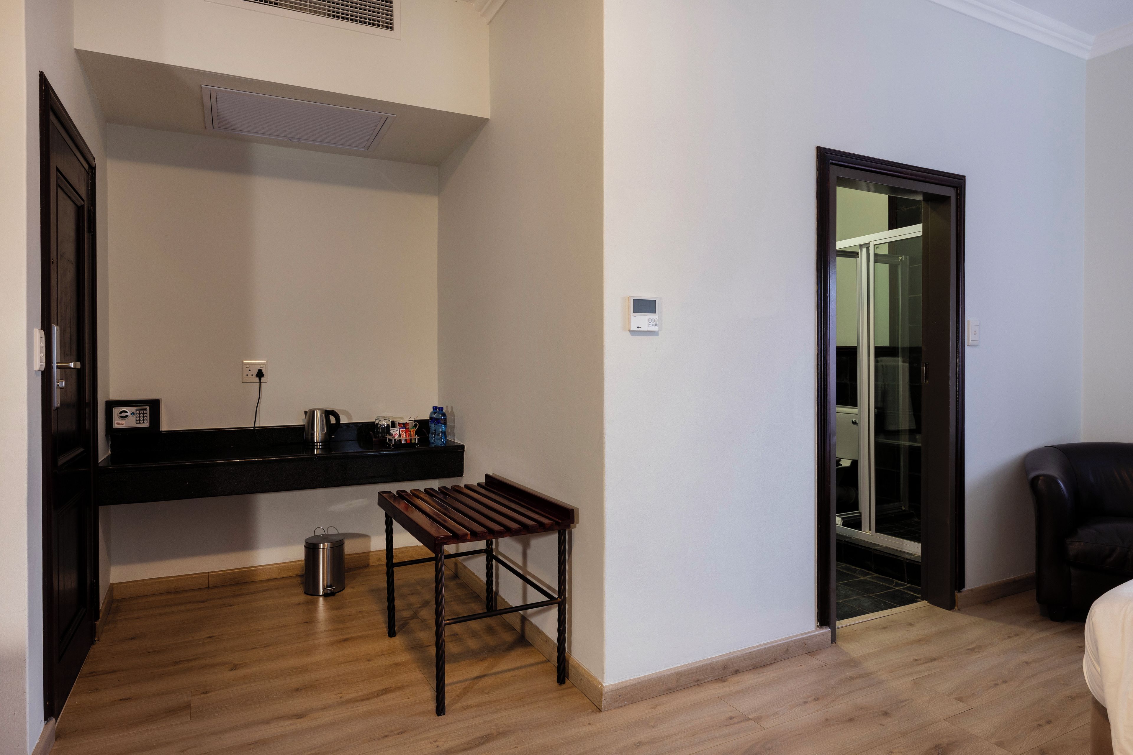 A room with a wooden floor, a black countertop with a kettle, a small table, a trash can, and a sliding glass door leading to another room.