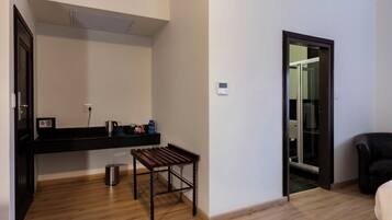A room with a wooden floor, a black countertop with a kettle, a small table, a trash can, and a sliding glass door leading to another room.