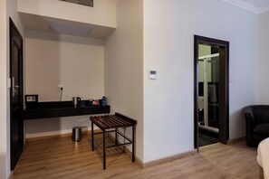 A room with a wooden floor, a black countertop with a kettle, a small table, a trash can, and a sliding glass door leading to another room. - Basden Wood Hotel Pty Ltd (Centurion)