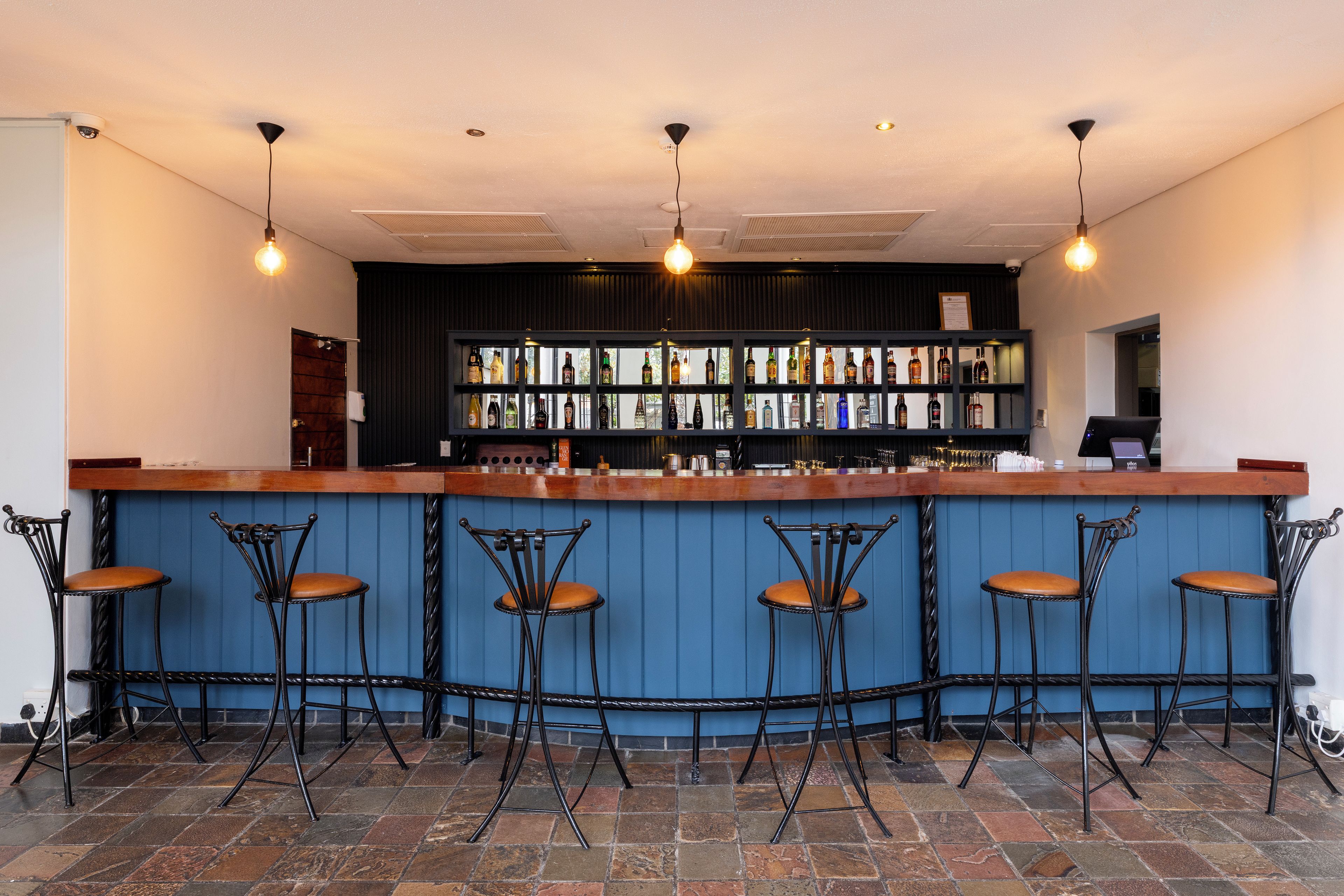 Um bar com balcão de madeira, banquetas de metal preto e parede azul.