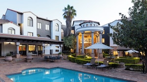 A pool area with a fountain, outdoor seating, and a building with columns.