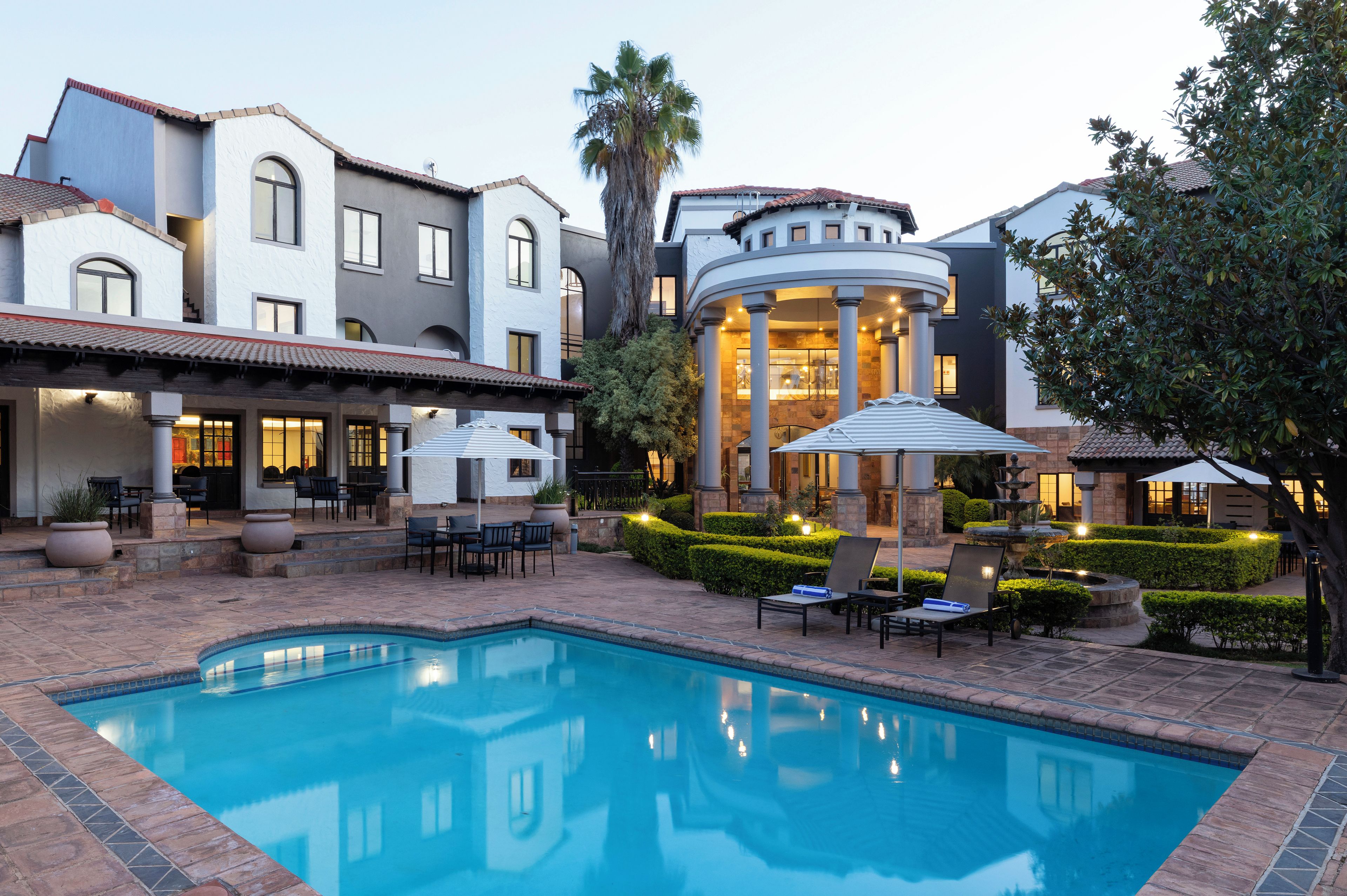 A pool area with a fountain, outdoor seating, and a building with columns.