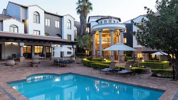 A pool area with a fountain, outdoor seating, and a building with columns.