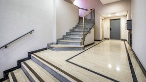 Ein modernes Hotelinterior mit einer Marmortreppe, einem ebenen Eingangsbereich und einer Tür zu einem weiteren Raum.