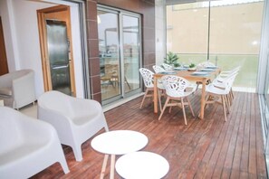 Un espacio interior moderno con una terraza de madera, sillas de plástico blanco y una mesa de comedor.