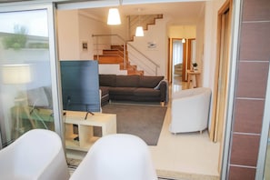 Una sala de estar moderna con un sofá, una mesa de centro y un mueble para televisión. Se ve una escalera que sube a un nivel superior.