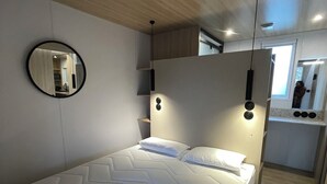 Quarto moderno com uma cama grande, espelho redondo e guarda-roupa embutido.