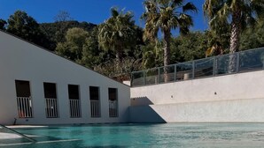 Piscina com água cristalina, rodeada por um edifício branco com janelas e varanda.
