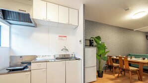 A modern kitchen with white cabinets, a built-in microwave, and a dining area with wooden chairs and a green couch. - 外観は古い建物ですが内装はフルリノベーション済みです。TV、無料Wi-Fi、ドライヤー、浴室乾燥機、洗濯機完備。トイレにはウォシュレットも完備しております。 (Nakamichi,Higashinari-ku,Osaka-shi)