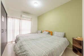 Een slaapkamer met een groot bed, een houten nachtkastje en een raam met gordijnen.