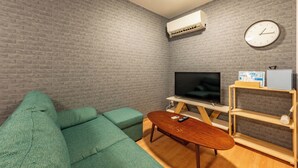 A living room with a green sofa, a wooden coffee table, a TV, and a clock on the wall. - 外観は古い建物ですが内装はフルリノベーション済みです。TV、無料Wi-Fi、ドライヤー、浴室乾燥機、洗濯機完備。トイレにはウォシュレットも完備しております。 (Nakamichi,Higashinari-ku,Osaka-shi)