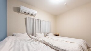 A bedroom with two beds, a nightstand, and an air conditioning unit. - 外観は古い建物ですが内装はフルリノベーション済みです。TV、無料Wi-Fi、ドライヤー、浴室乾燥機、洗濯機完備。トイレにはウォシュレットも完備しております。 (Nakamichi,Higashinari-ku,Osaka-shi)