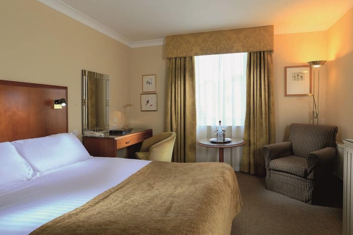 Habitación de hotel con una cama grande, un escritorio, una silla, una mesita y una ventana con cortinas.
