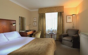 Habitación de hotel con una cama grande, un escritorio, una silla, una mesita y una ventana con cortinas.