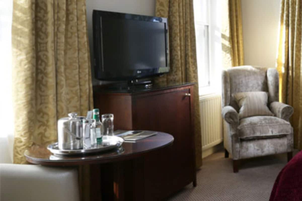 Una habitación de hotel con cama, televisión, silla y escritorio con una bandeja de objetos.