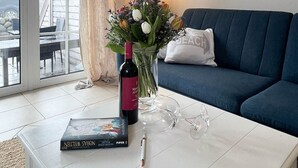 A modern living room with a white coffee table, a blue sofa, a lamp, a vase with flowers, a wine bottle, and a framed picture on the wall. - Amselkoje - Holiday apartment "Amselkoje" in Westerland is a real feel-good place (Sylt)