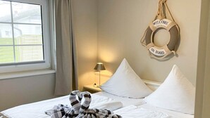 A neatly made bed with white linens, a striped towel, and a life preserver decoration on the wall. - Amselkoje - Holiday apartment "Amselkoje" in Westerland is a real feel-good place (Sylt)