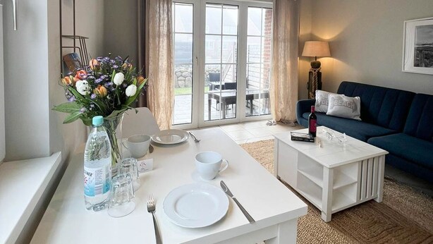 A modern living room with a dining area, a sofa, and a view through large windows. - Amselkoje - Holiday apartment "Amselkoje" in Westerland is a real feel-good place (Sylt)