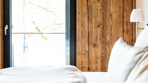 Ein Schlafzimmer mit Holzwand, einem Fenster und einem Bett mit weißer Bettwäsche.