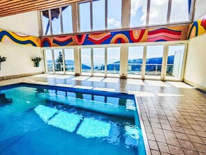 Piscina interior con vistas a montañas a través de amplios ventanales.