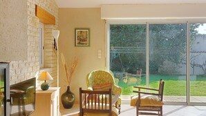 A cozy living room with a fireplace, a large window, and a view of the garden. - Le Château 3 by Interhome (Ile d'Oléron)
