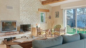 A living room with a stone wall, wooden beams, a fireplace, a TV, and a sofa. - Le Château 3 by Interhome (Ile d'Oléron)