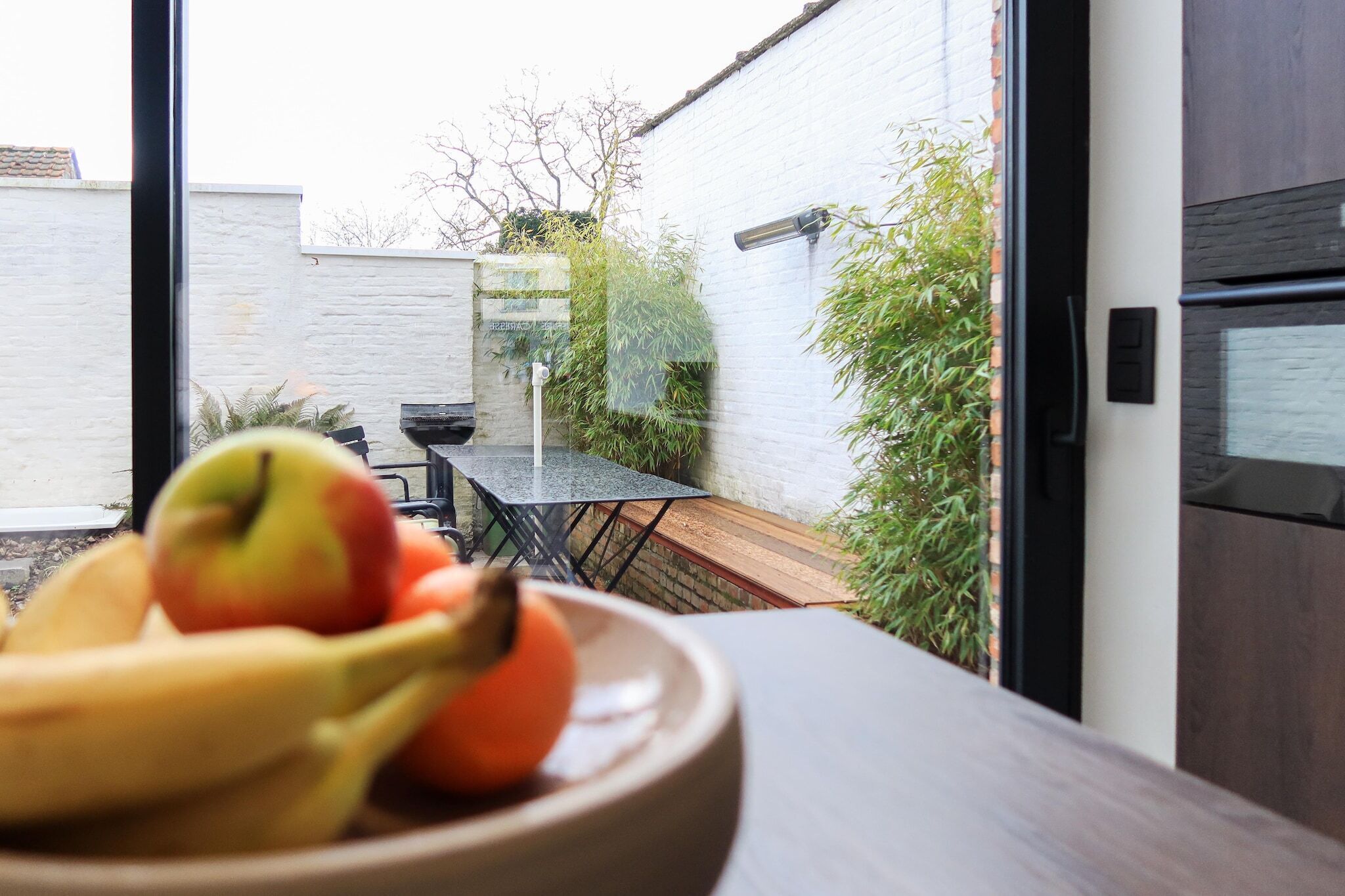 A bowl of fruit on a table with a view of a patio area.