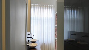 Ein Badezimmer mit zwei Waschbecken, einem Spiegel und einem Fenster mit Vorhängen.