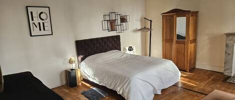 A bedroom with a large bed, a wooden wardrobe, a floor lamp, and a framed 'HOME' sign on the wall.