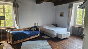 A room with a wooden floor, two beds, a small table, and a radiator. - Élégance Périgourdine (Beaumontois en Périgord)