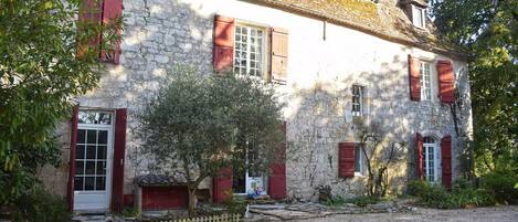 Un bâtiment en pierre avec des volets rouges et une allée gravillonnée.