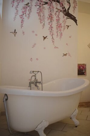 A clawfoot bathtub in a bathroom with a wall mural of cherry blossoms and birds. - Élégance Périgourdine (Beaumontois en Périgord)