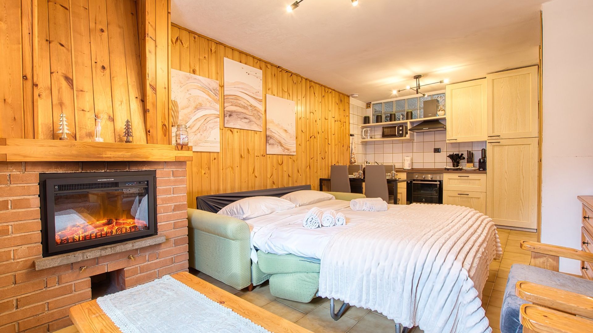 Ein gemütliches Zimmer mit Kamin, einem Bett, einer kleinen Küchenzeile und Holzwänden.