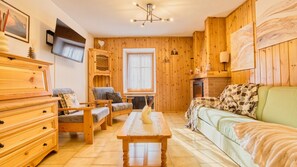 Ein gemütliches Zimmer mit Holzwänden, einem Kamin, einem Fernseher und einem großen Fenster.